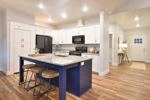 Kitchen featuring light stone counters, a kitchen bar, an island with sink, fridge with ice dispenser, and white cabinets