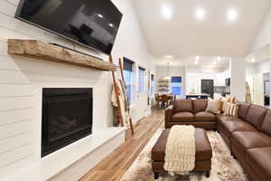 Living area featuring a fireplace with raised hearth, light wood finished floors, recessed lighting, a chandelier, and high vaulted ceiling
