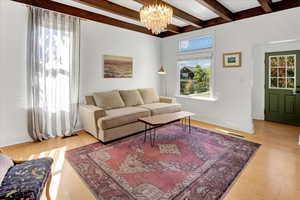 Living area featuring beam ceiling, light wood finished floors, and a chandelier
