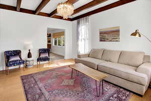 Living room with light wood finished floors, beamed ceiling, and a chandelier