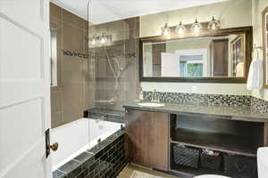 Bathroom featuring vanity, tiled shower / bath combo, and decorative backsplash