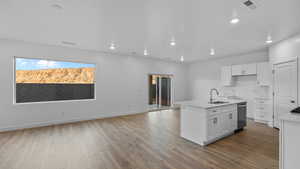 Kitchen featuring an island with sink, white cabinets, dark wood-style floors, light stone counters, and open floor plan