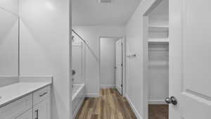 Bathroom featuring shower / bathtub combination, vanity, dark wood-style floors, and a walk in closet