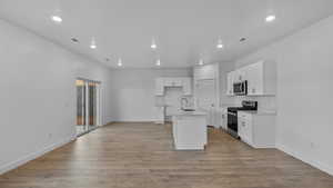 Kitchen with stainless steel appliances, white cabinetry, light wood finished floors, a center island with sink, and recessed lighting