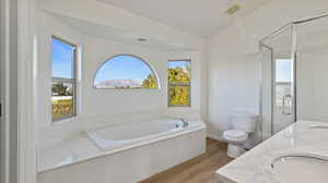 Bathroom featuring light wood-style floors, a garden tub, a shower stall, and double vanity