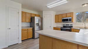 Kitchen featuring light countertops, stainless steel appliances, a peninsula, light wood-style flooring, and brown cabinetry