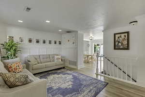 Living room with a decorative wall, light wood-type flooring, ornamental molding, wainscoting, and recessed lighting