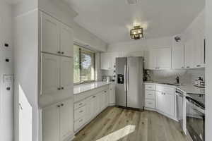 Kitchen featuring appliances with stainless steel finishes, white cabinetry, light wood-style flooring, decorative backsplash, and crown molding