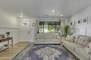 Living room featuring a decorative wall, a wainscoted wall, crown molding, wood finished floors, and recessed lighting