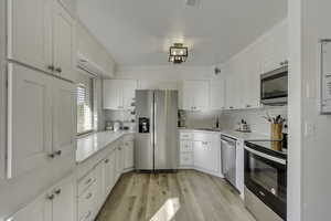 Kitchen featuring appliances with stainless steel finishes, light wood-type flooring, white cabinetry, decorative backsplash, and light stone counters