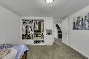 Bedroom with light colored carpet, a textured ceiling, a closet, and wooden walls