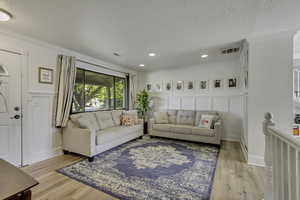 Living area featuring light wood-style flooring, ornamental molding, a decorative wall, and recessed lighting