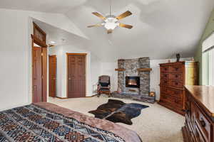 Bedroom with lofted ceiling, carpet floors, a stone fireplace, and a ceiling fan