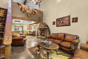 Living area with a towering ceiling, finished concrete flooring, and a stone fireplace