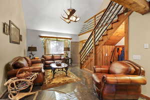 Living room featuring stairway, finished concrete flooring, lofted ceiling, a chandelier, and wooden walls