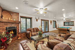 Living area featuring french doors, a textured ceiling, pool table, carpet floors, and a brick fireplace