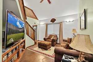 Living area featuring finished concrete floors, lofted ceiling, stairway, and a ceiling fan