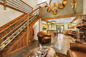 Living room featuring stairs, a warm lit fireplace, a chandelier, stone finish floors, and french doors