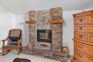 Living area with a stone fireplace, light colored carpet, and a textured ceiling