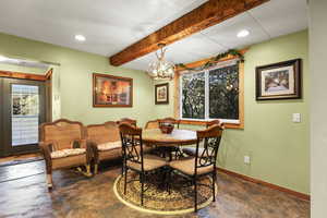 Dining space with beamed ceiling, a chandelier, concrete floors, and a textured wall