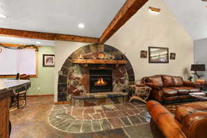 Living room featuring a stone fireplace and beam ceiling