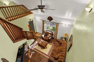 Living room featuring a textured ceiling, ceiling fan, stairway, and vaulted ceiling