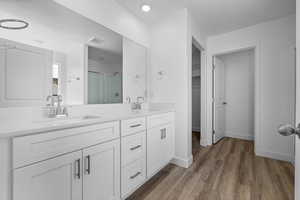 Full bathroom with a stall shower, double vanity, dark wood finished floors, and a walk in closet