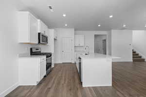 Kitchen featuring stainless steel appliances, white cabinets, dark wood finished floors, a center island with sink, and recessed lighting