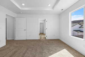 Unfurnished bedroom featuring a tray ceiling, light colored carpet, and recessed lighting