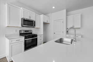 Kitchen featuring appliances with stainless steel finishes, white cabinets, light stone countertops, recessed lighting, and wood finished floors