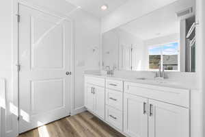 Full bath with double vanity, light wood finished floors, and recessed lighting