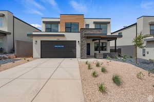 Contemporary home with driveway, stucco siding, stone siding, a garage, and covered porch