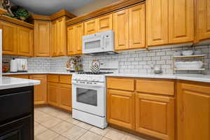 Kitchen with white appliances, light tile patterned floors, decorative backsplash, light cabinetry