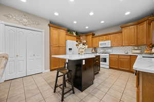 Kitchen featuring a kitchen bar, light stone countertops, light tile patterned floors, recessed lighting, double door pantry and tasteful backsplash