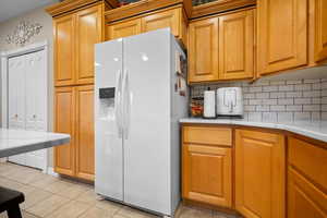 Kitchen featuring white refrigerator with ice dispenser, light tile patterned floors, tasteful backsplash, light cabinets