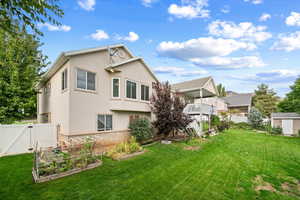 Rear view of property featuring stucco siding, a vegetable garden, a balcony, a shed, and brick siding
