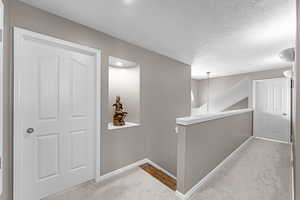 Corridor with carpet floors, a textured ceiling, and an upstairs landing