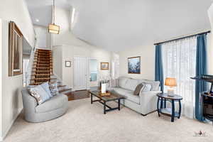 Living area with high vaulted ceiling, stairway, and light colored carpet