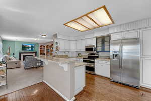 Kitchen with a breakfast bar, stainless steel appliances, white cabinetry, light wood-style floors, and a fireplace