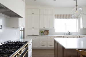 Kitchen featuring range with two ovens, custom range hood, white cabinetry, decorative light fixtures, and light stone countertops