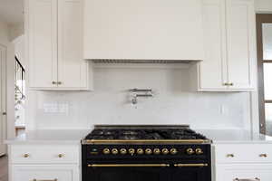 Kitchen featuring premium range hood, light stone countertops, range with two ovens, and white cabinets