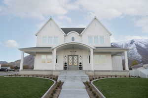View of front facade with a front yard, a mountain view, a porch, and roof with shingles