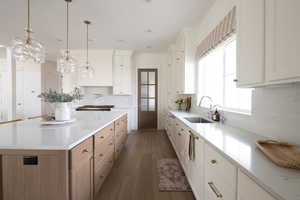 Kitchen featuring white cabinetry, pendant lighting, dark wood finished floors, a center island, and light stone counters