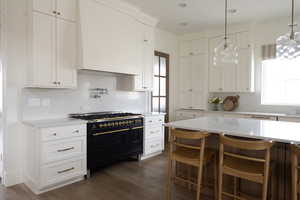Kitchen featuring double oven range, custom range hood, hanging light fixtures, white cabinets, and dark wood-style flooring