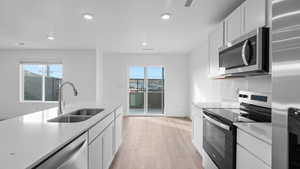 Kitchen featuring stainless steel appliances, white cabinets, light wood-type flooring, recessed lighting, and light stone counters