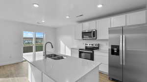 Kitchen with appliances with stainless steel finishes, light wood-style flooring, white cabinetry, an island with sink, and recessed lighting