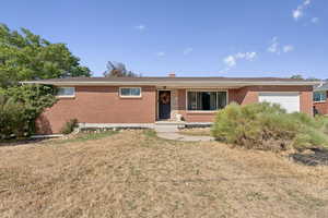 Single story home featuring brick siding, a garage, a front yard, and a chimney