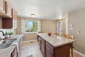 Kitchen featuring a breakfast bar, light stone counters, light tile patterned floors, a textured ceiling, and plenty of natural light