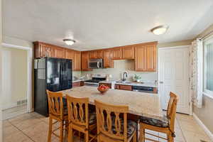 Kitchen featuring appliances with stainless steel finishes, a kitchen bar, light tile patterned floors, a textured ceiling, and light stone countertops