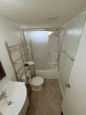 Full Bathroom with enclosed tub / shower combo, a textured ceiling, light tile patterned floors, and vanity